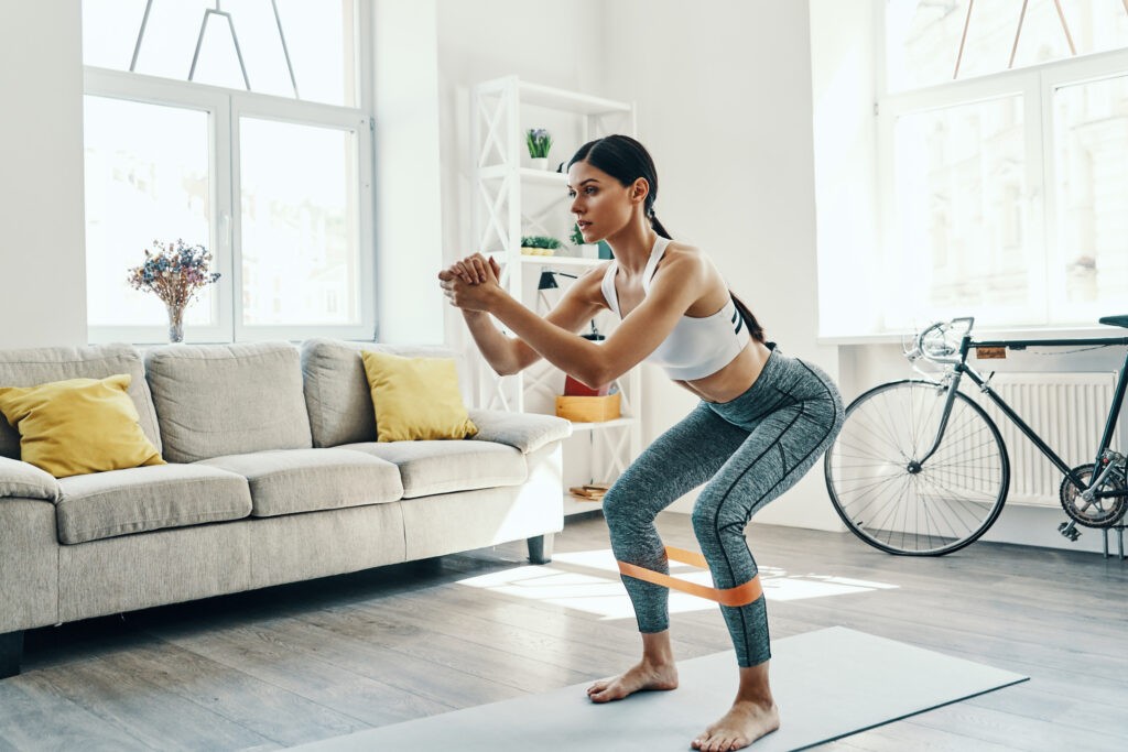Achieving best results. Beautiful young woman in sports clothing crouching while exercising at home